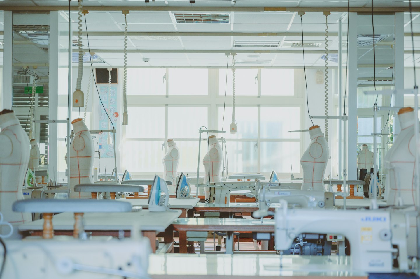 Rows of industrial sewing machines and mannequins in a clothing workshop.