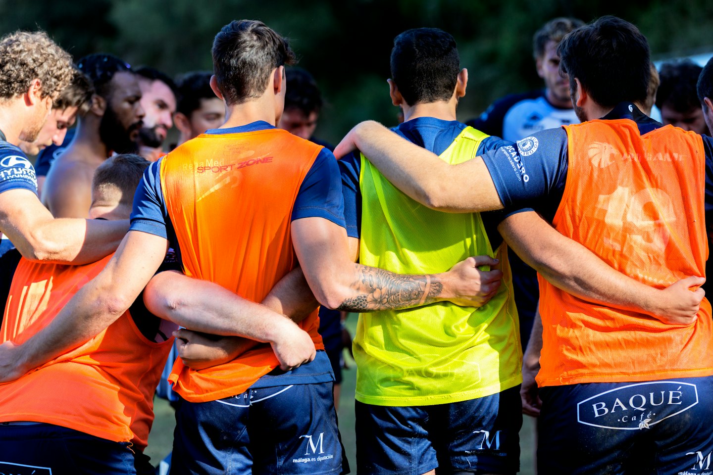 Athletes in training bibs huddle together on a sunny field.