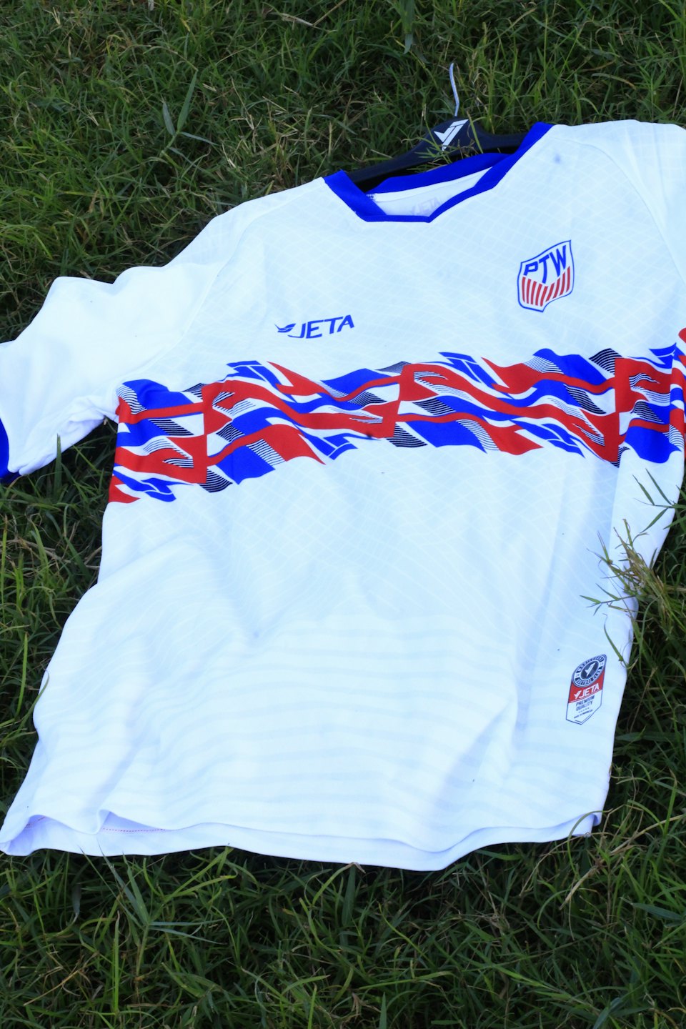 Sports jersey with colorful patterns lying on green grass.