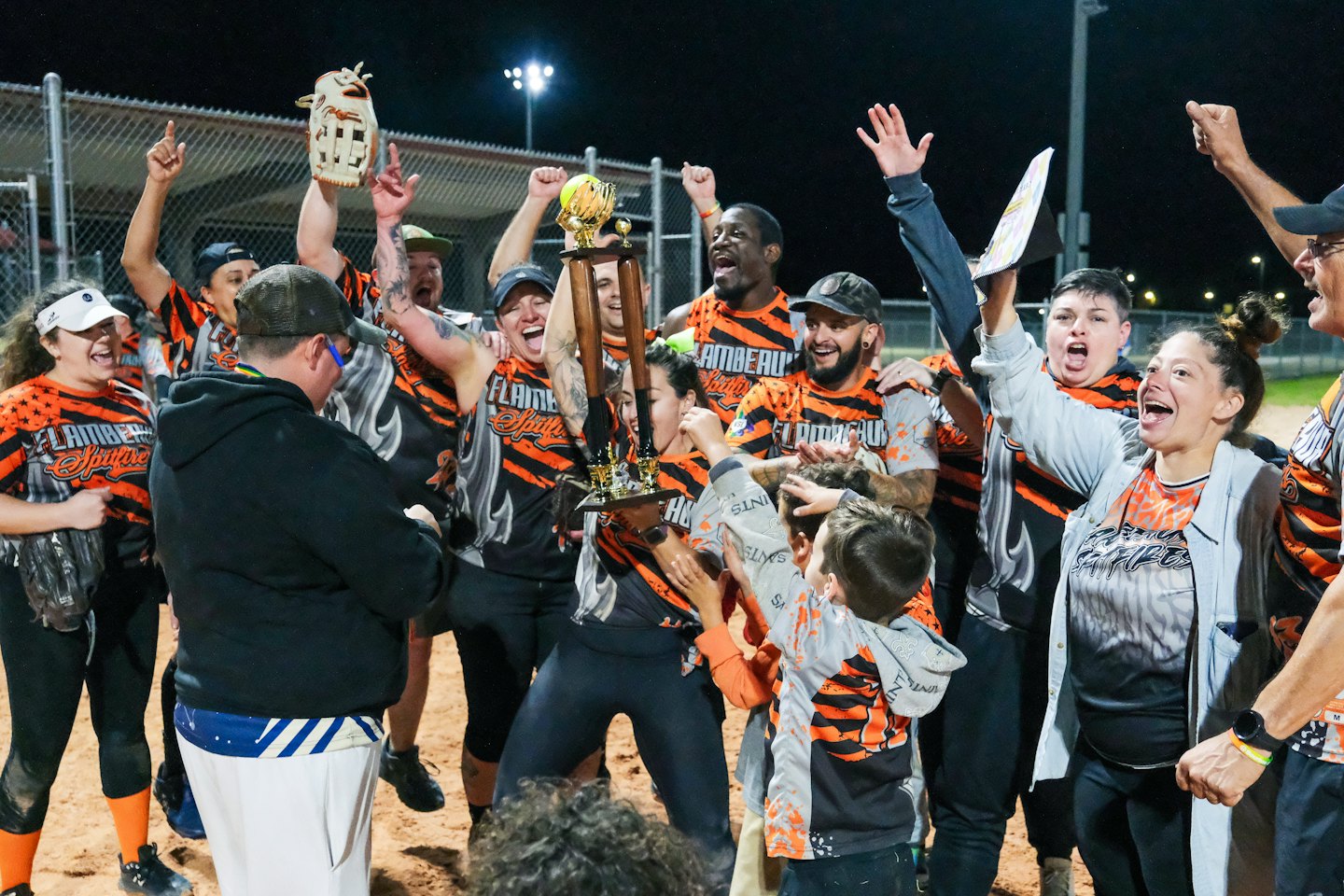 Softball team celebrates a victory by holding a trophy aloft.